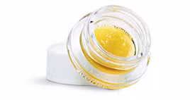 Small glass container with golden-yellow cannabis concentrate, shown at an angle with white lid beneath
